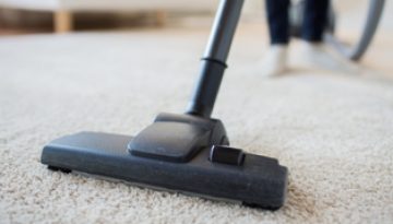 A vacuum cleaner head being passed over a lounge carpet.